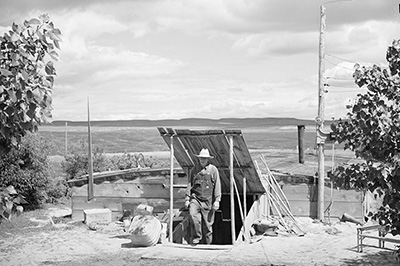 Man in overalls and a brimmed hat walks out of an underground shelter.