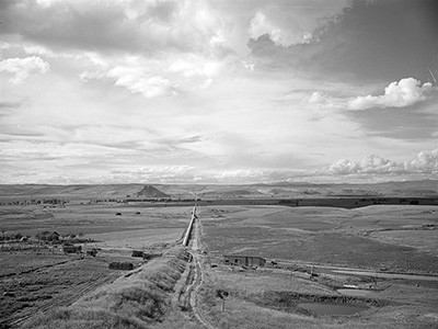 An irrigation pipe runs along farm land into the far distance. A dirt walking path parallels the pipe.