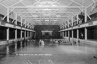 About 2 dozen people in a swimming pool housed in a wood building. Some of the people are in a canoe in the water.