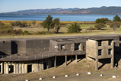 Two story stone structure. There are 4 window openings with bars across them horizontally and several doorway openings.