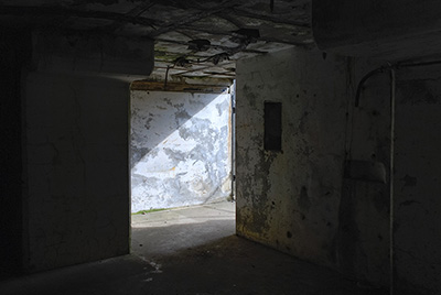 A dark stone room with sunlight shining in from a opening in the distance.