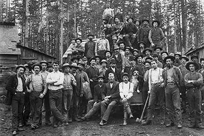 Dozens of men stand & sit while posing for a photo. One man holds an infant child. Several have musical insturments. 