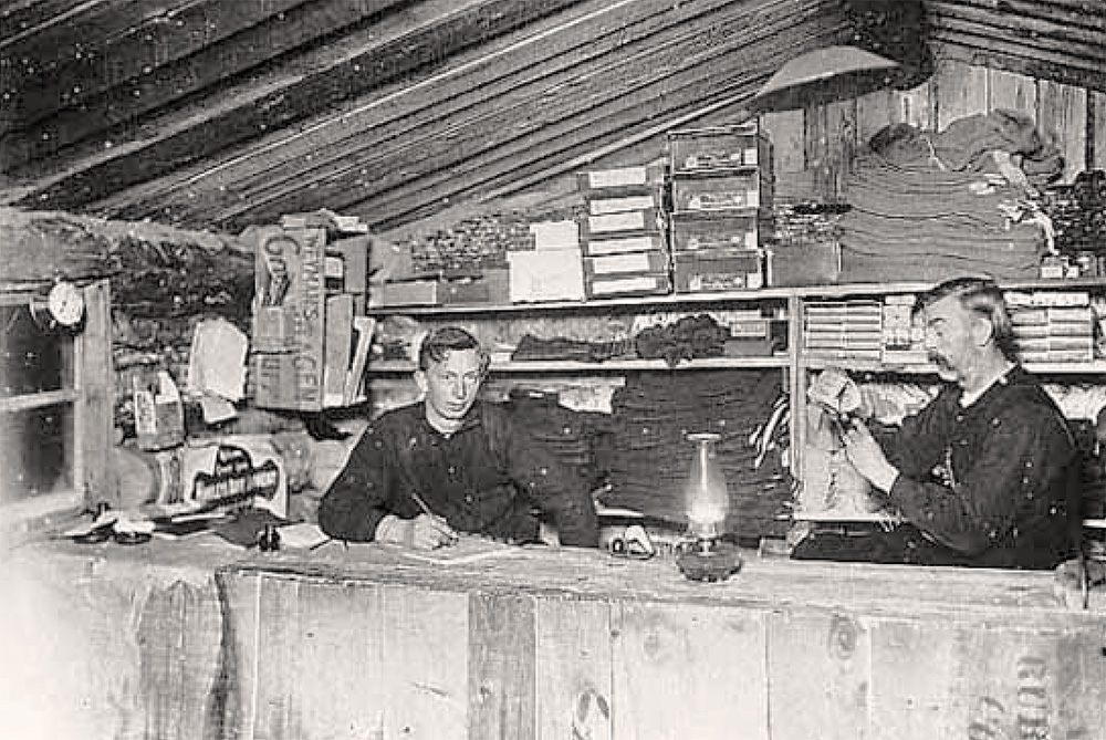 2 men stand behind a counter at a story in 1895.