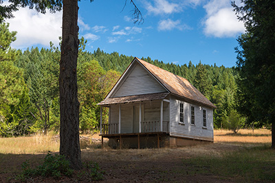 One-story wood-fram building with porch surrounded by trees. 