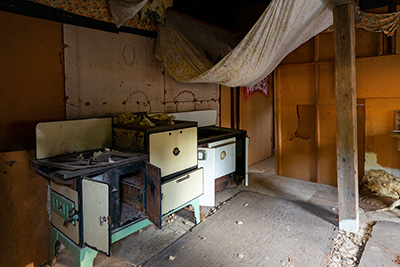 Living space contains old wood fired range with oven beside. Walls, ceiling & floor crumbling apart. 