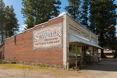 Brick building with metal awning in front. Mural on wall says "Welcome to the Sumpter Museum and Public Library."