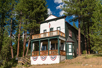 2 story wood house with balcony on 2nd level. Balcony serves as roof over porch below. Red white & blue banners hang on front.