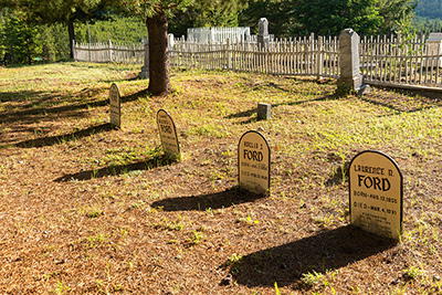 4 wood grave markers in a cemetery. All markers are for the Ford Family.  Laurence Ford was the postmaster and died in 1931