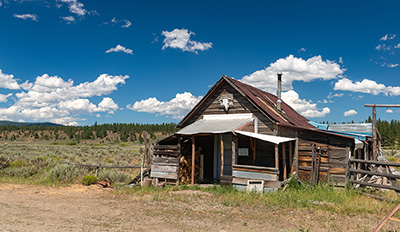 A run-down, falling down, plank building with a stove pipe coming out of the roof.