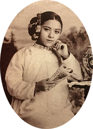 Photo of Tye Leung holding a book or paper in her right hand & smiling at the camera. Her hair is pulled into a bun on the right side of head.