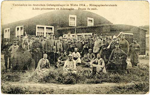 Dozens of men stand in a grassy area outside barracks.