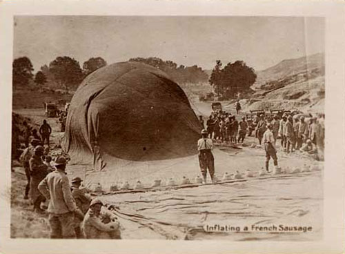 A crowd stands around a hot air balloon partially inflated laying on its side on the ground.