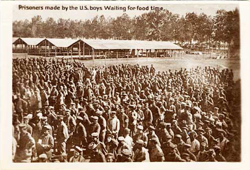 More than 100 men stnad in close lines in outdoor yard.