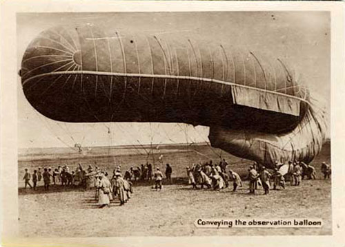 A hot air balloon about 30 ft off the ground is held by people holding tethers connected to it.