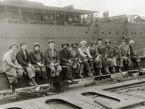 13 women rivet heaters take a break and sit along a metal girder