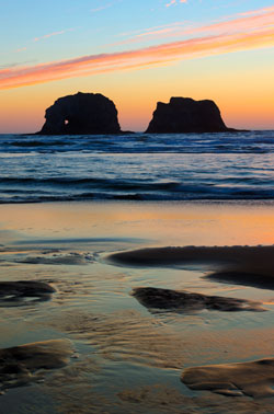 Two rock formations in the ocean at sunset.