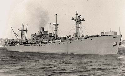 A Liberty ship seen in the water with smoke coming out of stack in background.