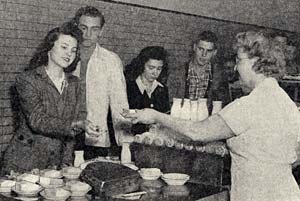 4 people lined up to get ice cream from a woman handing it out. 