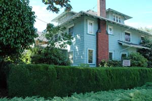 3 story home with attractive box hedge in front and mature trees in yard.