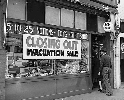 Store with sign "Closing out evacuation sale" and 2 people walking in front door.