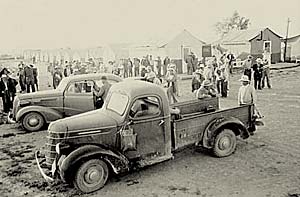 A truck & a car appear to load workers to transport them from the camp to the fields.