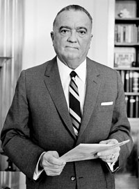 Photo of J. Edgar Hoover in suit and tie holding papers and looking at camera.