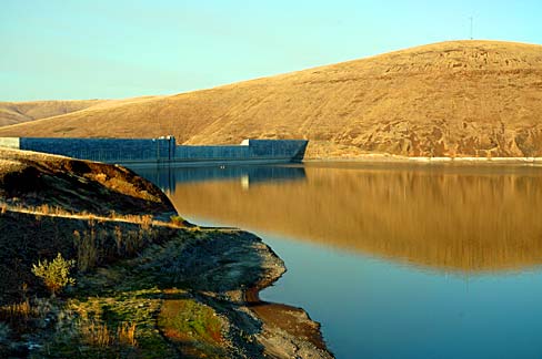 Golden brown hilside rolls down to a lake with a dam.