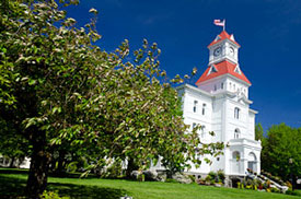 Benton County Courthouse with red roof on center tower. Green lawn and trees extend out from front.