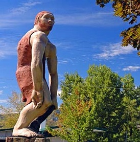 Fiberglass caveman statue with green trees in background and blue sky.