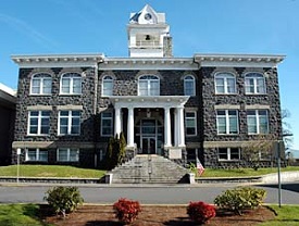 Three story stone building with 4 decorative columns framing front door and bell tower in center.