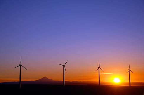 Four wind turbines shown with a colorful sunset in the background.