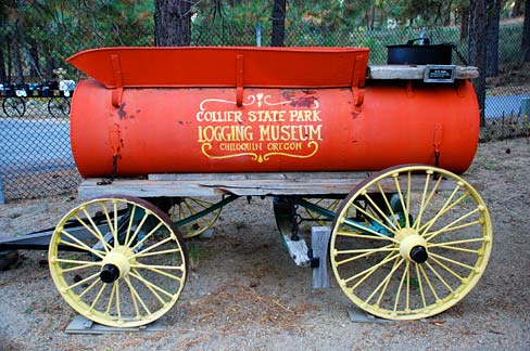 Antique logging equipment looks like a water tank on a flat wagon bed with wagon wheels. "Collier State Park Logging Museum" 