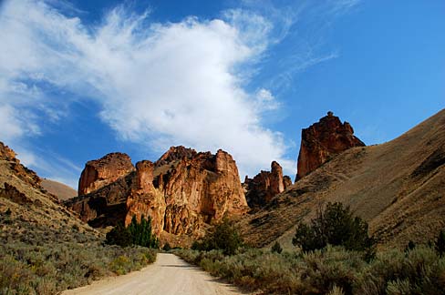 A well worn dirt path runs down the floor of a canyon. Interesting rock formations rise in the distance.