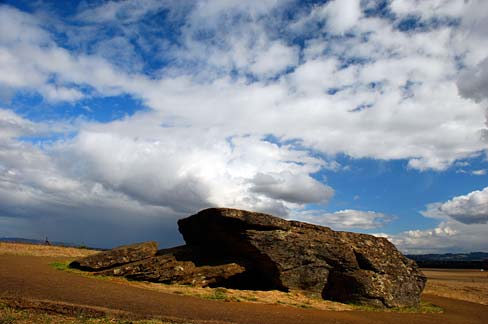 Rock in the middle of farmland. Blue sky and clouds in the background.