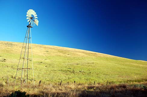 A weathered barn stands in a field with whispy clouds overhead in a blue sky. 