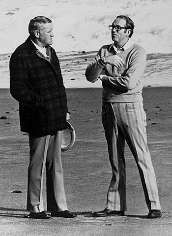 2 men stand on a beach facing each other. It appears they are discussing something.