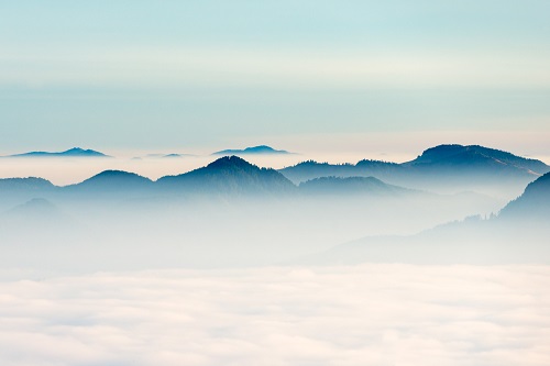 Tops of mountains peek above a layer of clouds below their tips.