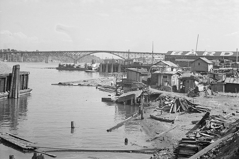 Shacks of plywood & any other material the builders could find are put together makeshift on a river bank. 