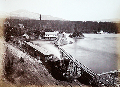 Train tracks lead over a tressle to a building situated on a lake side.