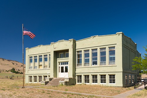 3 story brick building surrounded by yellowed grass and few trees.