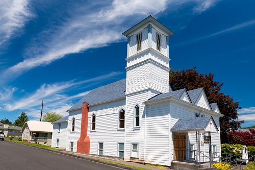 A 2 story church seen from the side with a brick chimney and a bell tower.