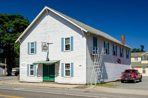 A 2 story building with wide front door with awning over door. Four windows on the front door side, 4 windows & a door on side.