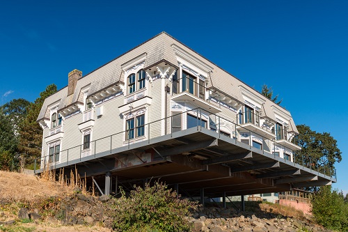 2 story house on a platform held to the side of a cliff with long projecting beam or girders.