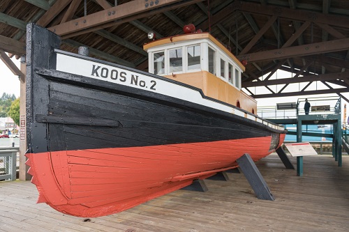 A tugboat held up by stilts on a wooden deck. The name on the side says "Koos No. 2".