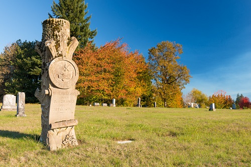 A stone pillar grave marker in a grassy field with other stone pillar grave markers in the distance.