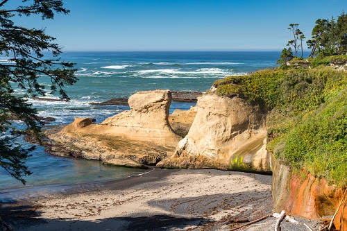 View from a bluff above the Pacific Ocean looks out over a rock formation which extends from the coast out into the water.