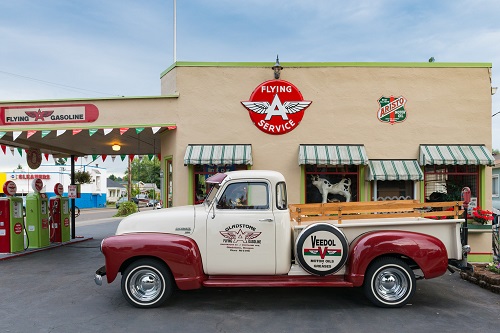 Gas station looks like late-1940s Flying A filling station with 3 porcelain pumps. A vintage truck is parked in front.