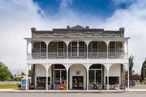 Two-story stone building with wrap-around porch on 2nd level. The porch serves as a covering for the sidewalk in front, as well has having its own roof.