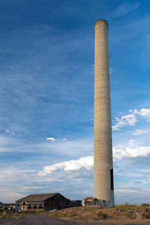 A smoke stack reaching 200 feet in the sky with a single story building near its base.