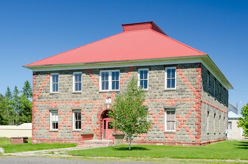 Two-story building made of blocks of local volcanic tuff. Painted with a red X design over gray stone. 